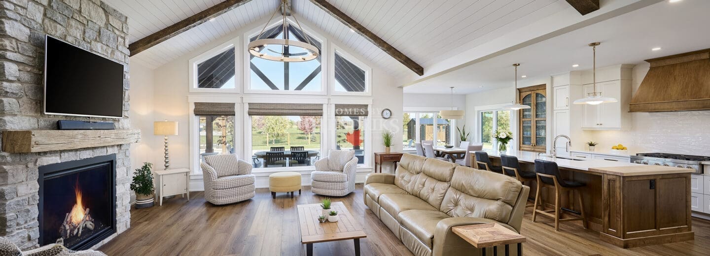A grand great room featuring stunning timber accents that add warmth and rustic charm to the space. The high ceilings are framed by exposed wooden beams, while large windows allow natural light to flood the room
