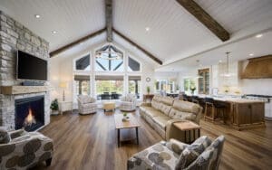 A grand great room featuring stunning timber accents that add warmth and rustic charm to the space. The high ceilings are framed by exposed wooden beams, while large windows allow natural light to flood the room