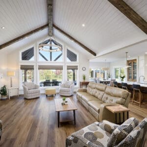A grand great room featuring stunning timber accents that add warmth and rustic charm to the space. The high ceilings are framed by exposed wooden beams, while large windows allow natural light to flood the room