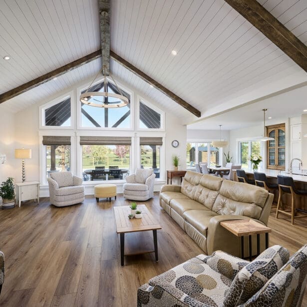 A grand great room featuring stunning timber accents that add warmth and rustic charm to the space. The high ceilings are framed by exposed wooden beams, while large windows allow natural light to flood the room