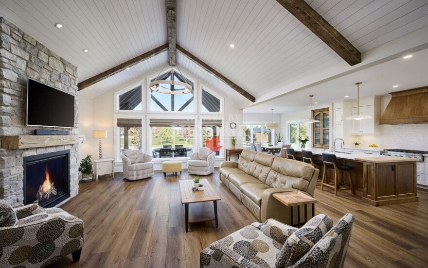 A grand great room featuring stunning timber accents that add warmth and rustic charm to the space. The high ceilings are framed by exposed wooden beams, while large windows allow natural light to flood the room